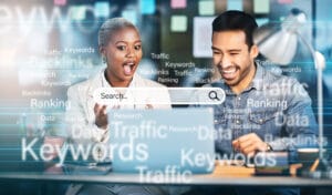 Two colleagues at a desk view a screen with SEO terms like Keywords, Backlinks, and Traffic around a large search bar.
