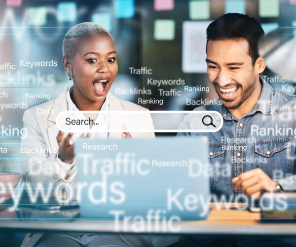 Two colleagues at a desk view a screen with SEO terms like Keywords, Backlinks, and Traffic around a large search bar.